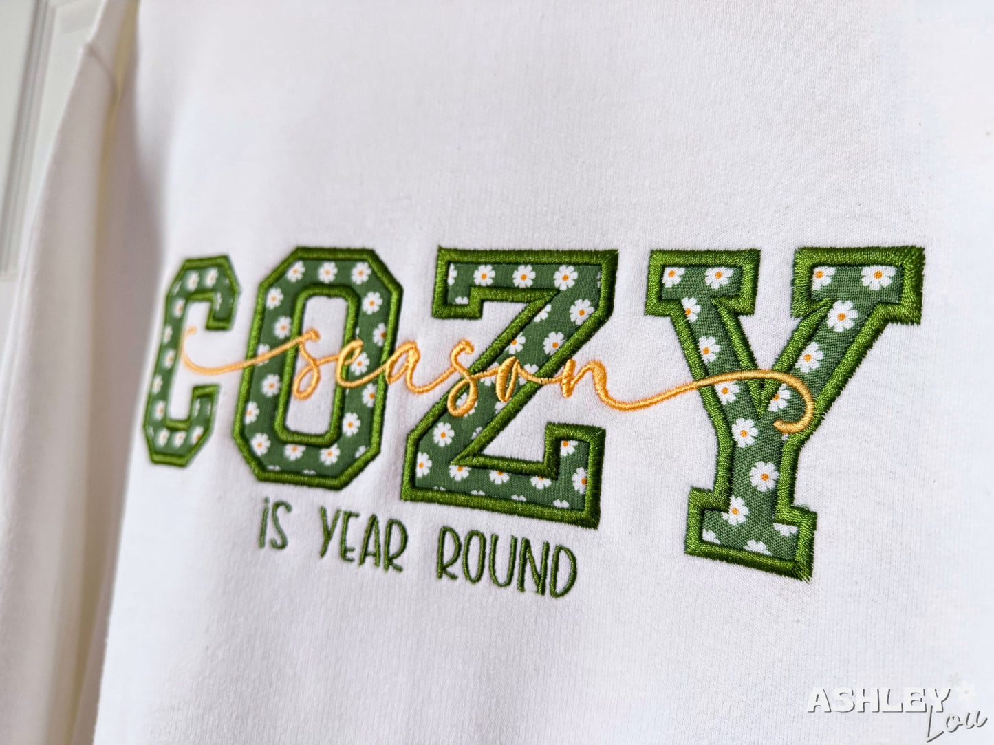 Embroidered text on a white background with 'COZY season is year round' and floral details.