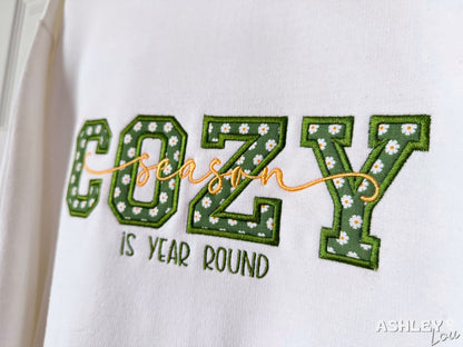 Embroidered text on a white background with 'COZY season is year round' and floral details.